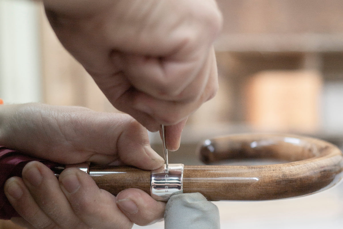 A craftsman's hands fitting a curved wooden umbrella handle by hand in a London workshop