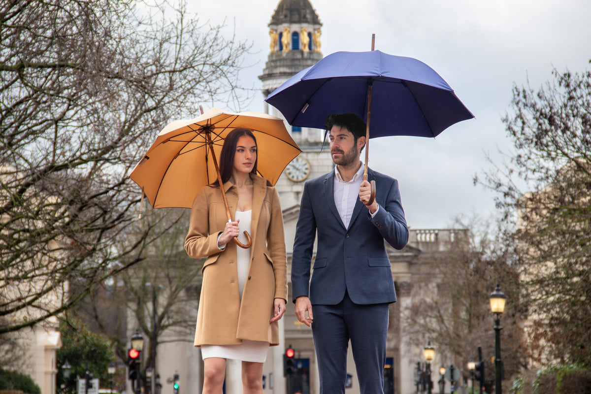 A man and a woman in London carrying Bucklesbury umbrellas in navy and camel, with a clock tower behind