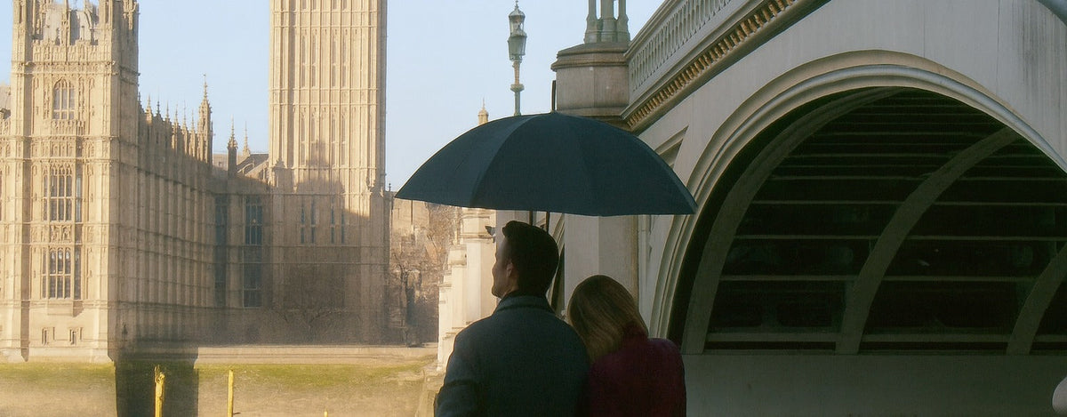 A couple sharing a dark umbrella beside Westminster Bridge, with the Houses of Parliament and Big Ben behind them in London