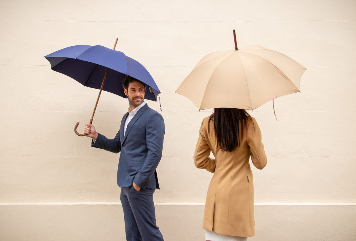 A man and a woman with Bucklesbury umbrellas against a white stone wall in London