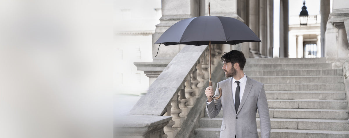Man in een grijs pak met een zwarte Bucklesbury London Umbrella met handvat en steel uit één stuk hout