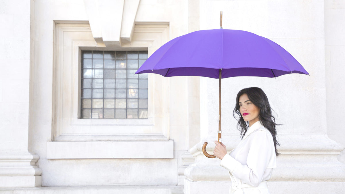 Woman holding a purple Bucklesbury umbrella beside a stone window at the Old Royal Naval College, Greenwich